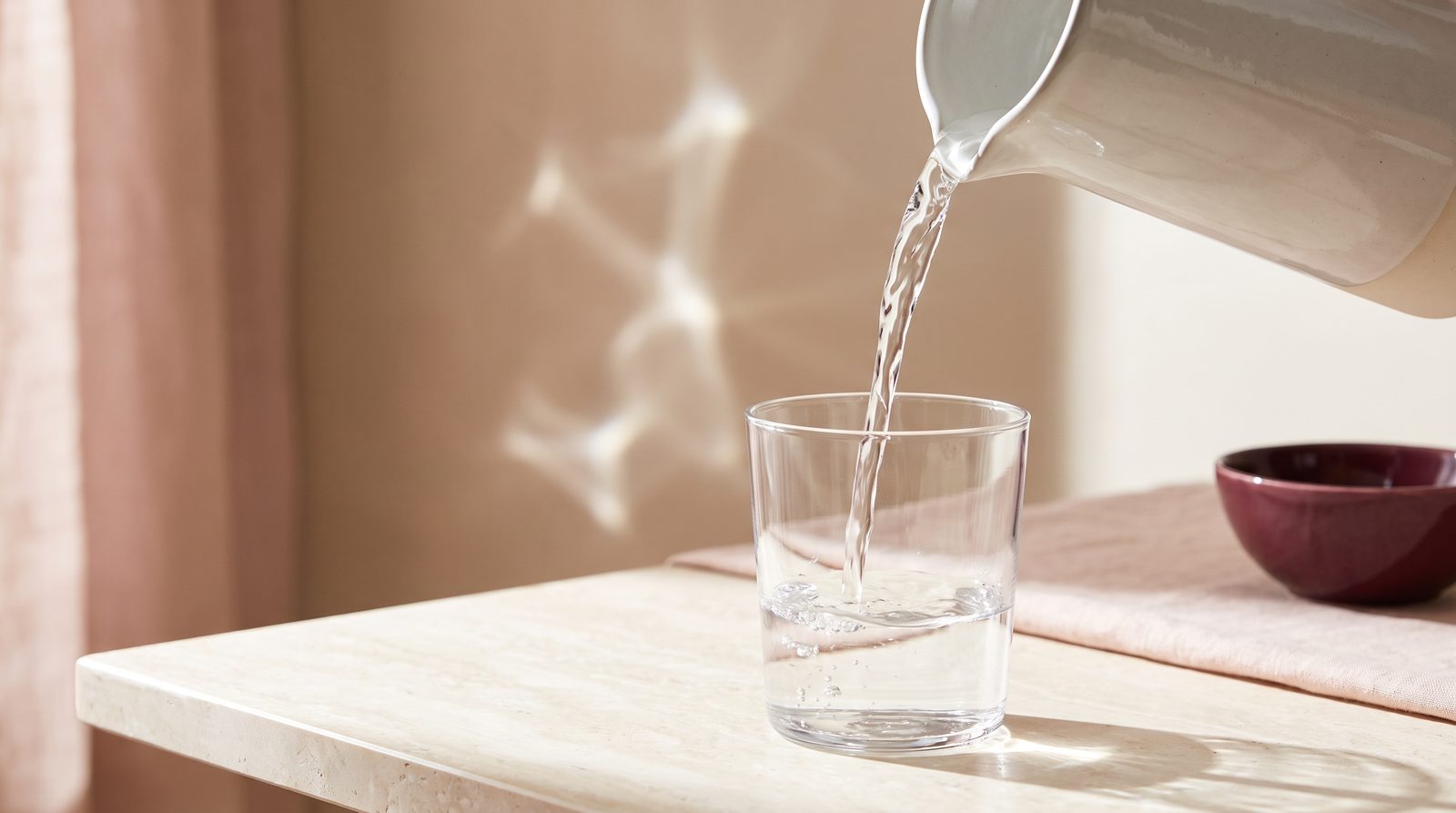 Clear water being poured from a jug into a plain glass in soft daylight